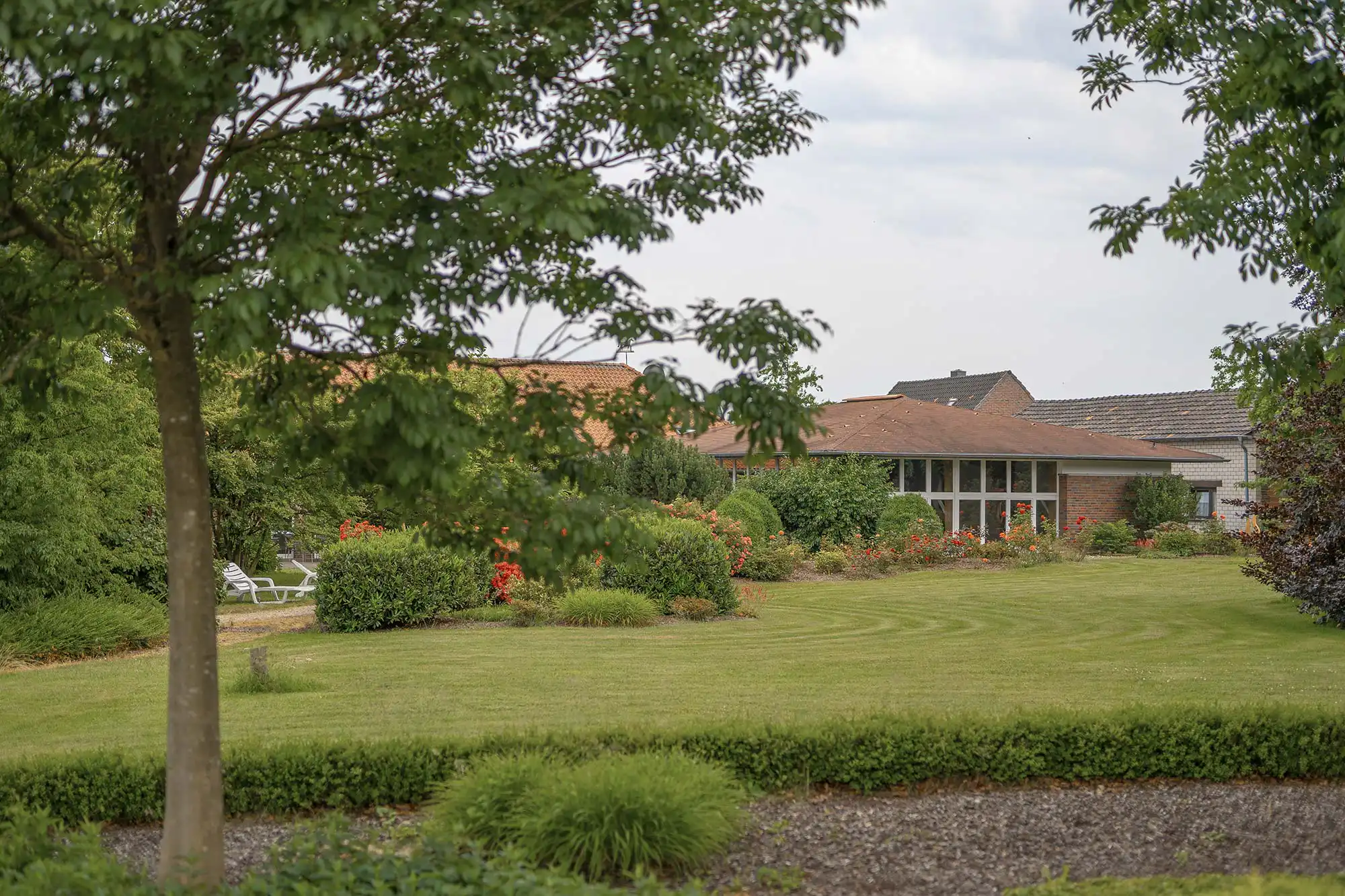 privatklinik-fuer-psychosomatik-nrw Eine gepflegte Gartenanlage mit grüner Wiese und blühenden Büschen umgibt ein modernes Gebäude und vermittelt eine ruhige, einladende Atmosphäre.